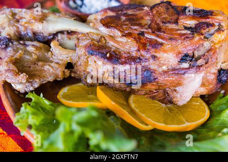 Gros plan de délicieux porc rôti avec laitue, tranches d'orange et haricots réfrits sur un bol en argile. Viande savoureuse et accompagnements au-dessus de la patte orange et rouge Banque D'Images