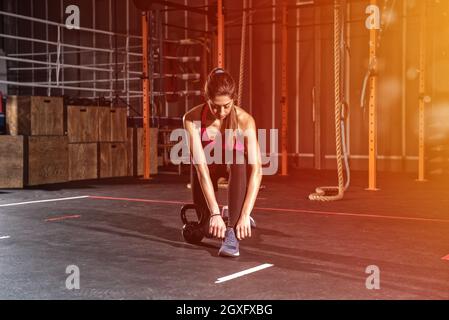 Une jeune fille athlétique déterminée prête à commencer des exercices avec une kettlebell à la salle de gym Banque D'Images