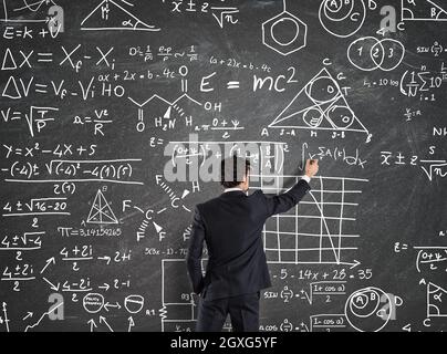 Homme d'affaires essayant de résoudre des problèmes avec les calculs mathématiques sur le tableau noir Banque D'Images