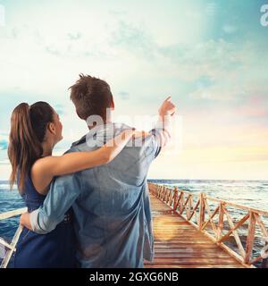 Couple of lovers points to the sky on a pier at sunset Stock Photo