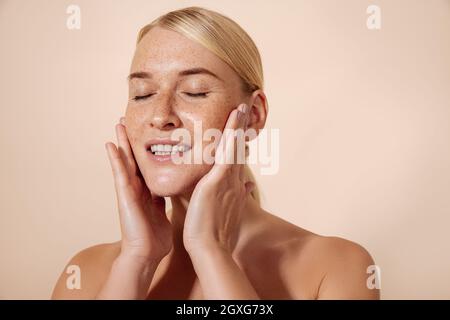 Photo studio d'une jeune femme blonde touchant son visage avec les yeux fermés et souriant Banque D'Images