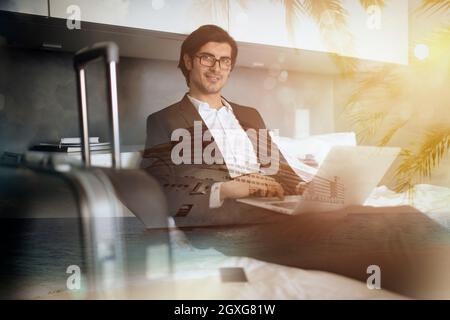 Homme d'affaires voyageur à la maison avec son ordinateur portable prêt pour les vacances en bateau de croisière. Double exposition Banque D'Images