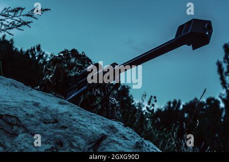 Tireur d'élite de l'armée avec un grand fusil couché en attente dans la forêt la nuit. Vue en angle bas, prise de vue en diagonale Banque D'Images