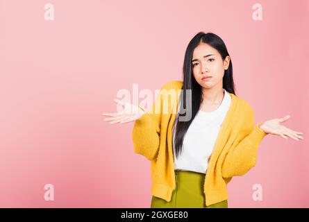 Portrait asiatique beau mignon jeune femme adolescent haussant avec propagation les mains qu'elle a choqué ne comprennent pas et confus studio tourné isolé sur fond rose Banque D'Images