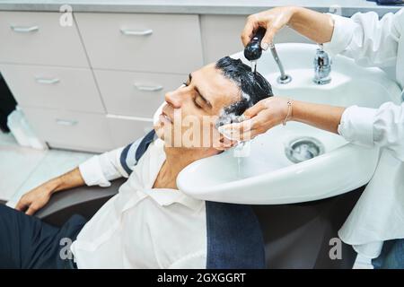 Coiffeur vaporisant de l'eau sur les cheveux d'un client détendu Banque D'Images