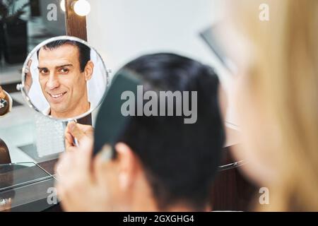 Homme dans un salon de coiffure qui vérifie sa coupe de cheveux dans le miroir Banque D'Images