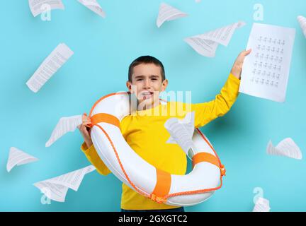 Un jeune garçon malheureux étudiant se noye dans une mer de feuilles d'exercices. Fond cyan Banque D'Images