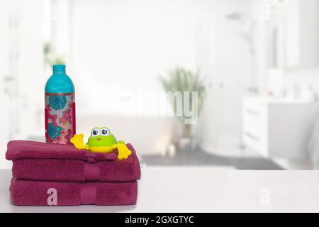 Table sur fond de serviettes. Gros plan d'une pile ou d'une pile de serviettes de bain en éponge violet avec un adoucisseur de lavage et une grenouille drôle sur le bain flou Banque D'Images