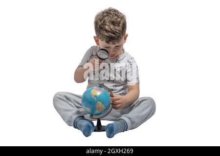 Garçon regardant à travers la loupe au globe, isolé sur fond blanc. École, concept d'éducation. Banque D'Images