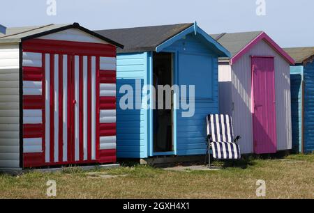 Cabanes de plage colorées en bord de mer avec chaise longue vide, Dovercourt Bay, Harwich, Essex, Angleterre, ROYAUME-UNI Banque D'Images