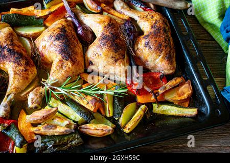 Repas familial sain avec des cuisses de poulet rôties et des légumes cuits au four servis sur une plaque de cuisson Banque D'Images