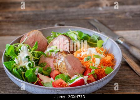 Plat avec filet de porc et délicieux mélange de salade.Servi dans un bol avec un couteau et une fourchette isolés sur une table en bois.Dîner à faible teneur en glucides ou cétogène Banque D'Images