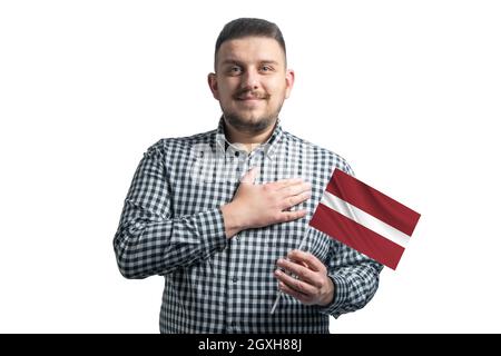 Homme blanc tenant un drapeau de la Lettonie et tient sa main sur son coeur isolé sur un fond blanc avec amour à la Lettonie. Banque D'Images