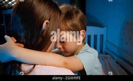 Portrait d'un petit garçon mécontent et triste qui embrasse et embrasse sa mère avant d'aller dormir la nuit. Parents et enfants aimant et bienveillants. Banque D'Images