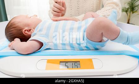 Une jeune mère qui s'occupe de lui a fait caresser son petit nouveau-né, son fils, tout en le pesant sur une balance numérique à l'hôpital. Concept de l'hygiène des bébés et nouveau-nés et h Banque D'Images