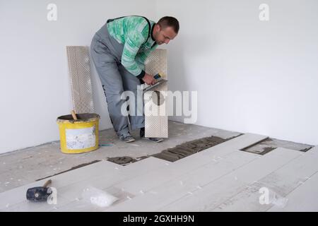 Travailleur qualifié installer les tuiles en céramique sur le sol travailleur fabriquer des planchers laminés sur le chantier du nouvel appartement Banque D'Images