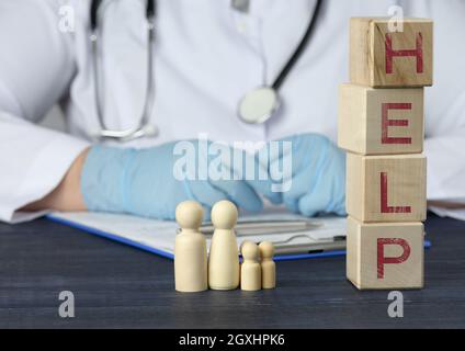 les figures en bois des hommes et l'inscription aident sur les cubes en bois, derrière la table se trouve un médic. Concept de soins médicaux, assurance, confiance Banque D'Images