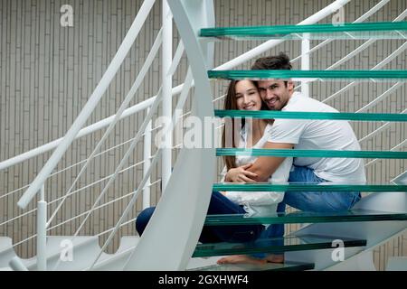 Jeune couple détendue sur verre escaliers en spirale à l'intérieur villa maison moderne Banque D'Images