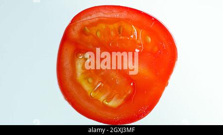 Gros plan de la tranche de tomate rouge dans l'eau sur fond blanc. Arrière-plan abstrait des légumes et des fruits Banque D'Images