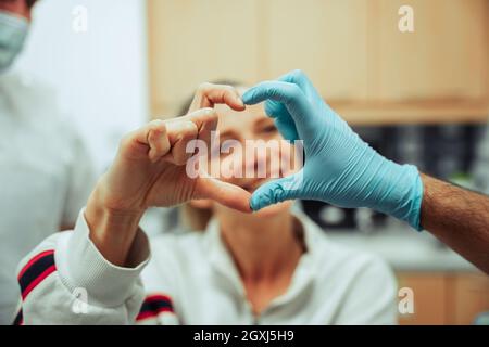 Femelle caucasienne de l'adolescence appréciant le contrôle mensuel au dentiste formant la forme du coeur avec les mains avec le médecin Banque D'Images