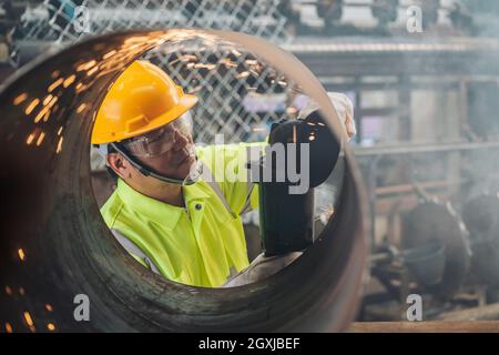 Un travailleur asiatique travaille en usine sur le meulage de roues électriques sur des tuyaux en acier. Banque D'Images