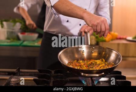 Young male chef mettre les épices sur les légumes dans le wok à cuisine commerciale Banque D'Images