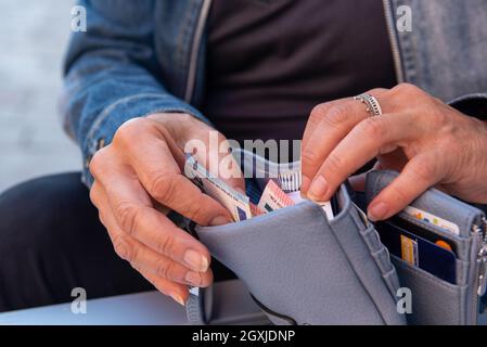 Fille prend un billet de banque de son portefeuille en cuir bleu appuyé contre une petite table.Gros plan sur les mains, l'argent et le portefeuille. Banque D'Images