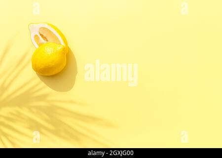 Deux demi-morceaux de citron avec ombre de la feuille de palmier sur fond jaune. Concept de saine alimentation, de voyage ou de vacances Banque D'Images