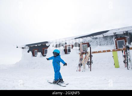 un tout-petit garçon dans un casque, des lunettes de protection, une combinaison bleue se tient à skier sur une pente de montagne enneigée. Cours de ski pour enfants à l'école de ski. Active en hiver Banque D'Images