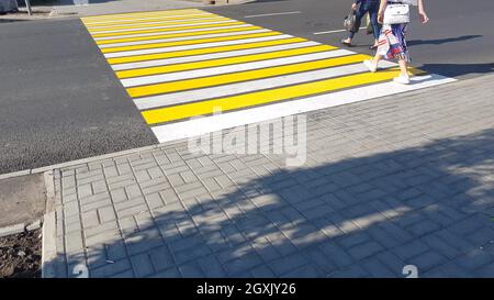 deux piétons franchissent la route sur un nouveau marquage jaune-blanc d'un concept de passage à niveau, de sécurité de la vie, de transport. Banque D'Images