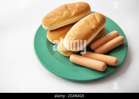 Petits pains chauds frais qui se trouvent sur une assiette verte avec des saucisses. Vue de dessus, gros plan Banque D'Images