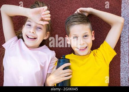 Thème de style de vie de sport pour enfants. Les jeunes garçons et filles heureux s'étendent joyeusement sur la couverture en caoutchouc de la piste de course du stade et s'effacent dans l'appareil photo avec le sourire Banque D'Images