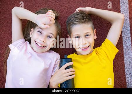 Thème de style de vie de sport pour enfants. Les jeunes garçons et filles heureux s'étendent joyeusement sur la couverture en caoutchouc de la piste de course du stade et s'effacent dans l'appareil photo avec le sourire Banque D'Images