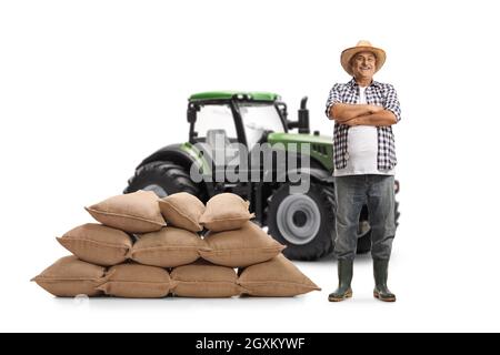 Portrait complet d'un agriculteur mûr se posant à côté d'un tracteur vert isolé sur fond blanc Banque D'Images