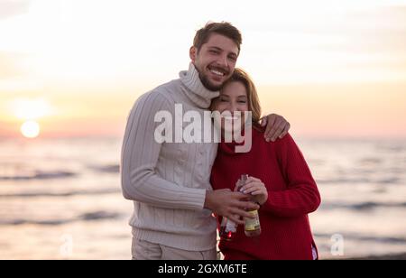 Jeune couple hugging et boire de la bière sur le coucher du soleil au cours de l'automne temps at beach Banque D'Images