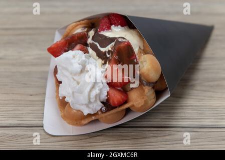 Le cornet de gaufres se régle avec des fraises en tranches et est recouvert de crème fouettée pour un dessert parfaitement sucré. Banque D'Images