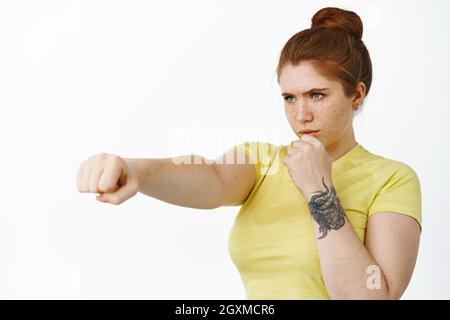 Portrait d'une fille de forme physique grave de tête rouge, étirez-vous le poing fermé, faire l'entraînement de boîte, les exercices de boxe d'ombre, arrière-plan de whtie Banque D'Images