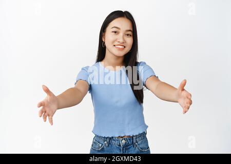 Belle fille asiatique porter, tenir quelque chose, étirant les mains vides, debout dans un t-shirt décontracté sur fond blanc Banque D'Images