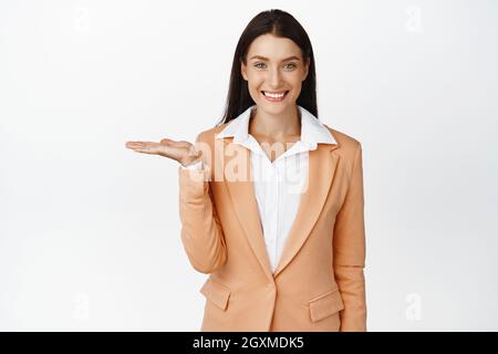 Une vendeuse souriante montre le produit sur une paume vide. Bonne femme d'affaires montrant sur la main, debout en costume, publicité, debout en costume contre Banque D'Images