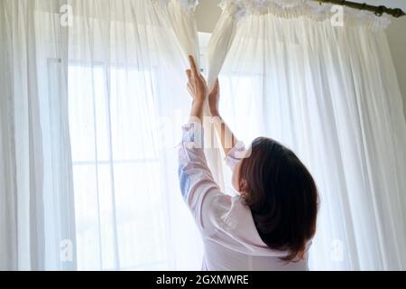 Gros plan de la main de femme ouvrant et fermant des rideaux translucides légers Banque D'Images