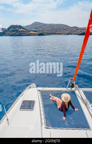 Jeune femme avec chapeau assis dans le filet d'un catamaran de voile, voyage de voile, Rhodes, Dodécanèse, Grèce Banque D'Images