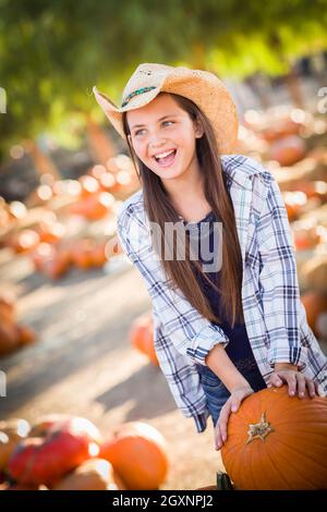 Preteen Girl Wearing Cowboy Hat jouant avec une brouette à la citrouille dans un cadre rustique de pays. Banque D'Images