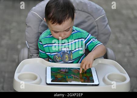 Tout-petit, 2 ans, multiethnique, eurasien, assis en chaise haute et jouant à un jeu éducatif sur tablette, Stuttgart, Baden-Wuerttemberg, Allemagne Banque D'Images