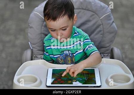 Tout-petit, 2 ans, multiethnique, eurasien, assis en chaise haute et jouant à un jeu éducatif sur tablette, Stuttgart, Baden-Wuerttemberg, Allemagne Banque D'Images