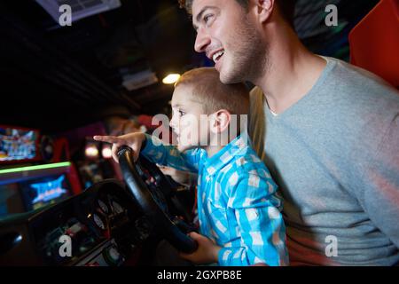 Heureux père et fils jouer roue de conduite en aire de jeux vidéo theme park Banque D'Images