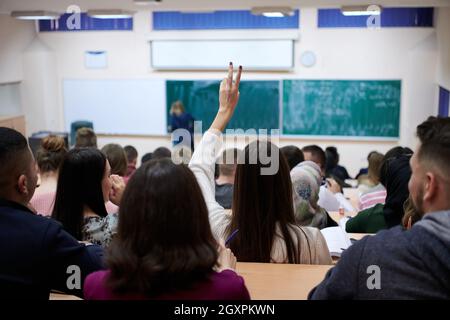 Vue arrière de l'élève assis dans la classe et la main pour poser une question au cours d'une conférence. High school student soulève de part et demande de conférencier Banque D'Images