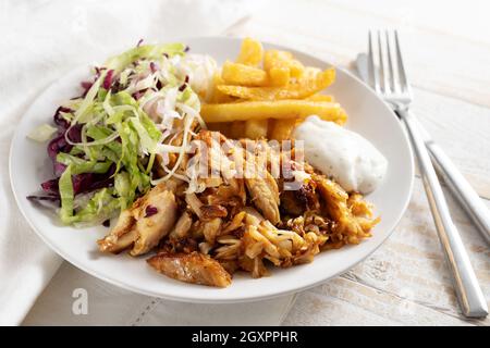 Donner de la viande de poulet kebab aux frites, salade et sauce tzatziki sur une assiette blanche, couverts et serviette sur une table en bois rustique, sélection, narr Banque D'Images