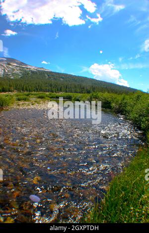 Burbling creek avec des rochers coupe à travers un pâturage vert avec une montagne et le ciel bleu en arrière-plan Banque D'Images