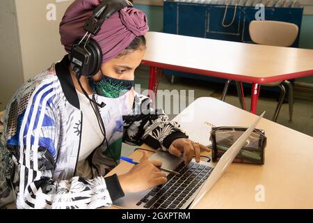 Éducation secondaire étudiante travaillant sur un ordinateur portable en classe, portant un casque et un masque facial pour protéger contre le virus Covid-19 Banque D'Images