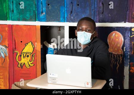 Éducation secondaire étudiant de sexe masculin à la recherche d'un ordinateur portable en classe, portant un masque facial pour protéger contre l'infection Covid-19 Banque D'Images